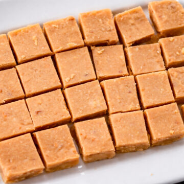 easy peanut butter fudge squares neatly arranged on a white plate, smooth and creamy homemade fudge pieces with a soft, slightly crumbly texture