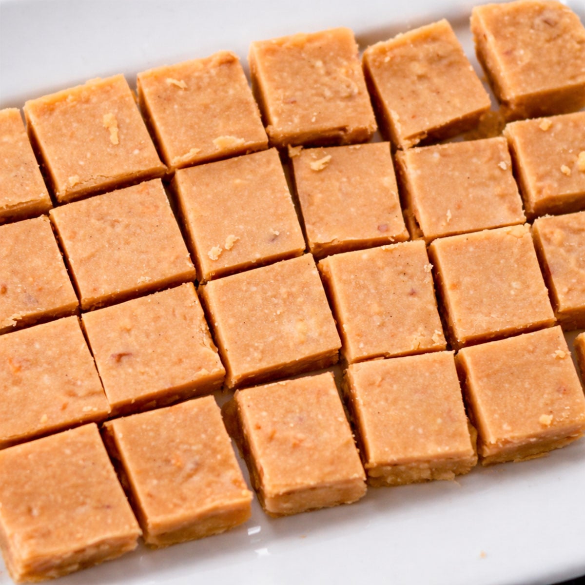 easy peanut butter fudge squares neatly arranged on a white plate, smooth and creamy homemade fudge pieces with a soft, slightly crumbly texture