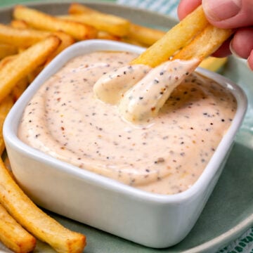 Close-up of crispy fries being dipped into creamy pepper mayonnaise in a white bowl on a green plate