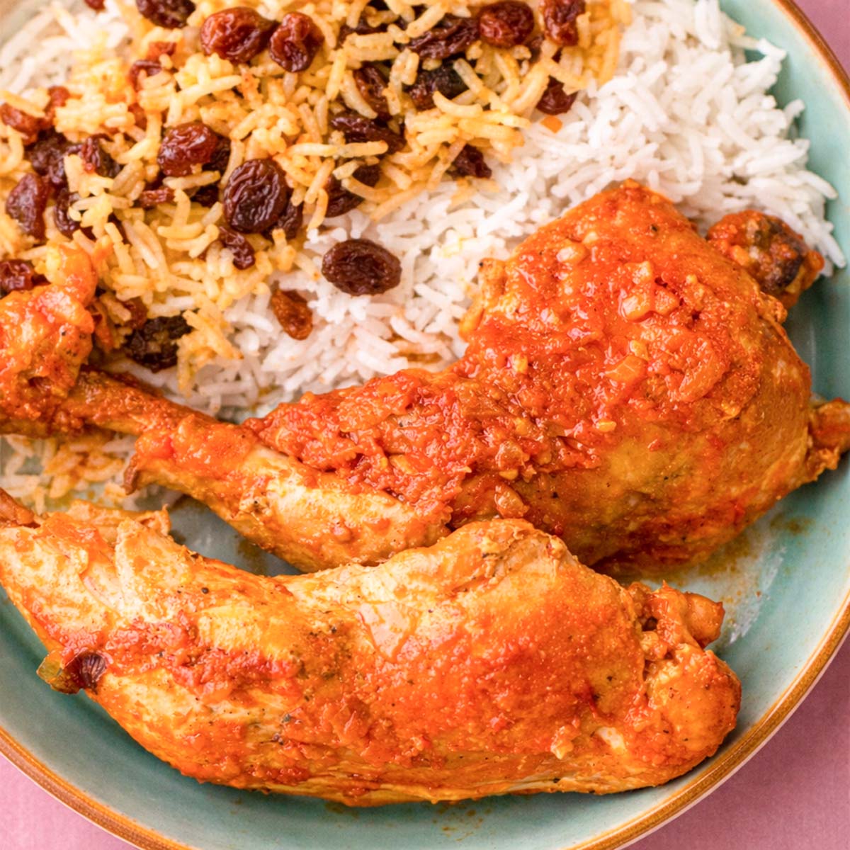 Persian chicken in tomato sauce with fluffy saffron rice and sweet raisins, served in a bowl with the sauce spooned over the chicken.