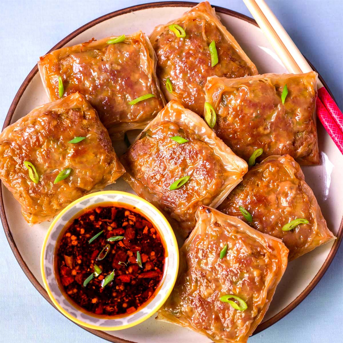 Crispy rice paper dumplings served on a plate with chili oil dipping sauce and sliced green onions