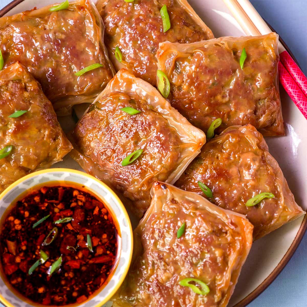 Rice paper dumplings on a plate with chili oil dipping sauce and green onion garnish