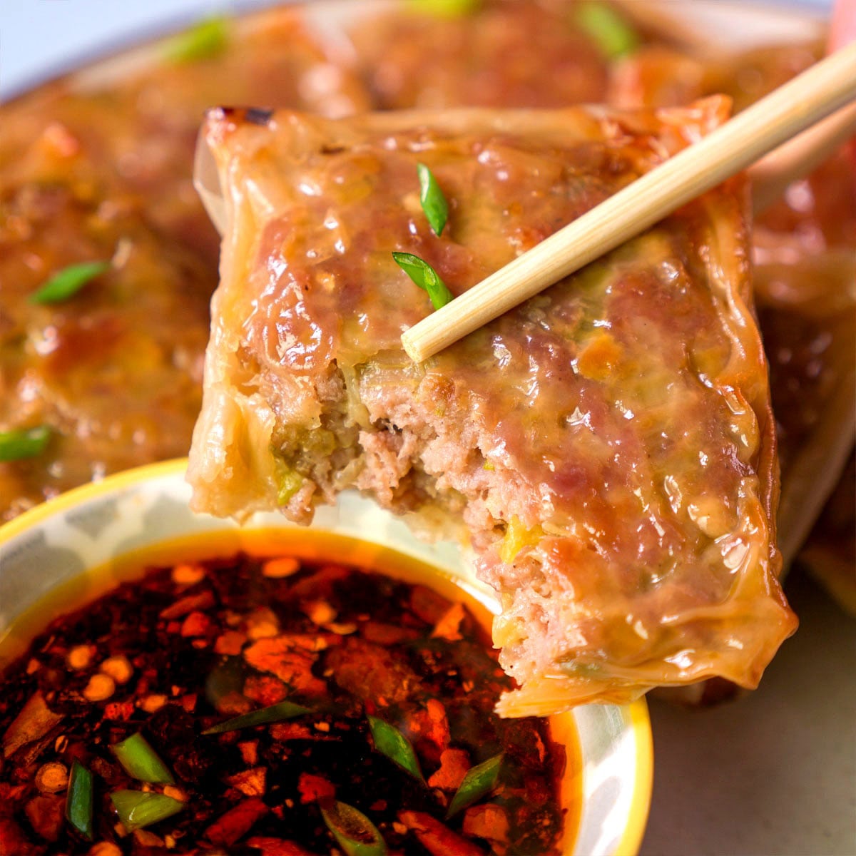 Rice paper dumpling with pork filling held by chopsticks over a bowl of chili oil dipping sauce
