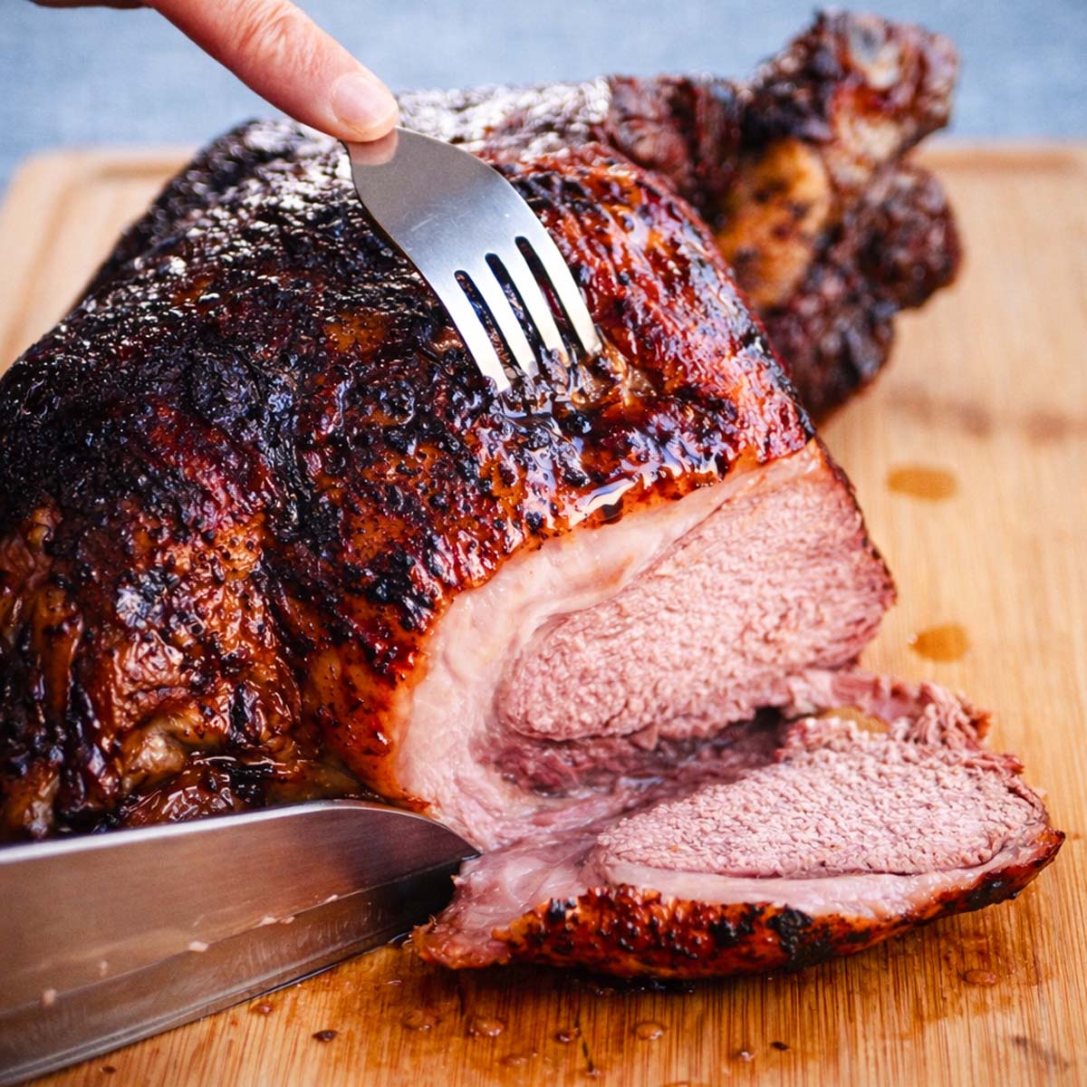 Sliced roast leg of lamb on a wooden board, showing a browned crust and tender, juicy meat as it's being carved.