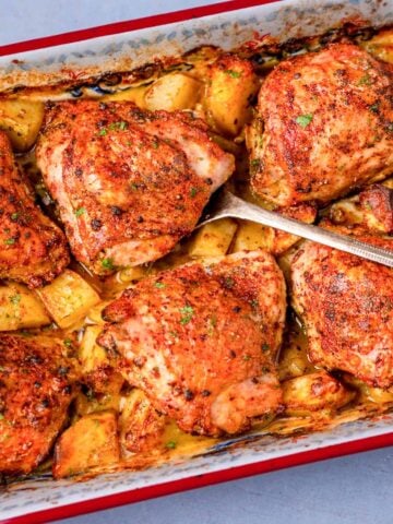 One pan roasted chicken thighs and potatoes baked until golden and crispy in a roasting dish.