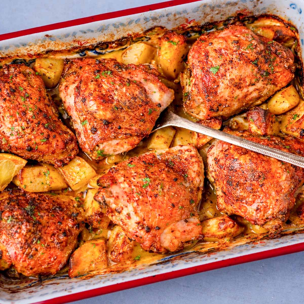 One pan roasted chicken thighs and potatoes baked until golden and crispy in a roasting dish.