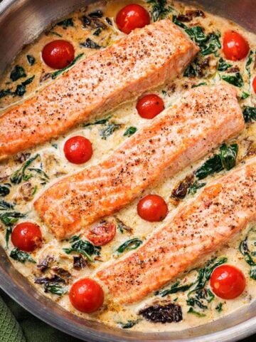 Salmon Florentine cooked in a skillet with creamy spinach sauce, cherry tomatoes, and parmesan.