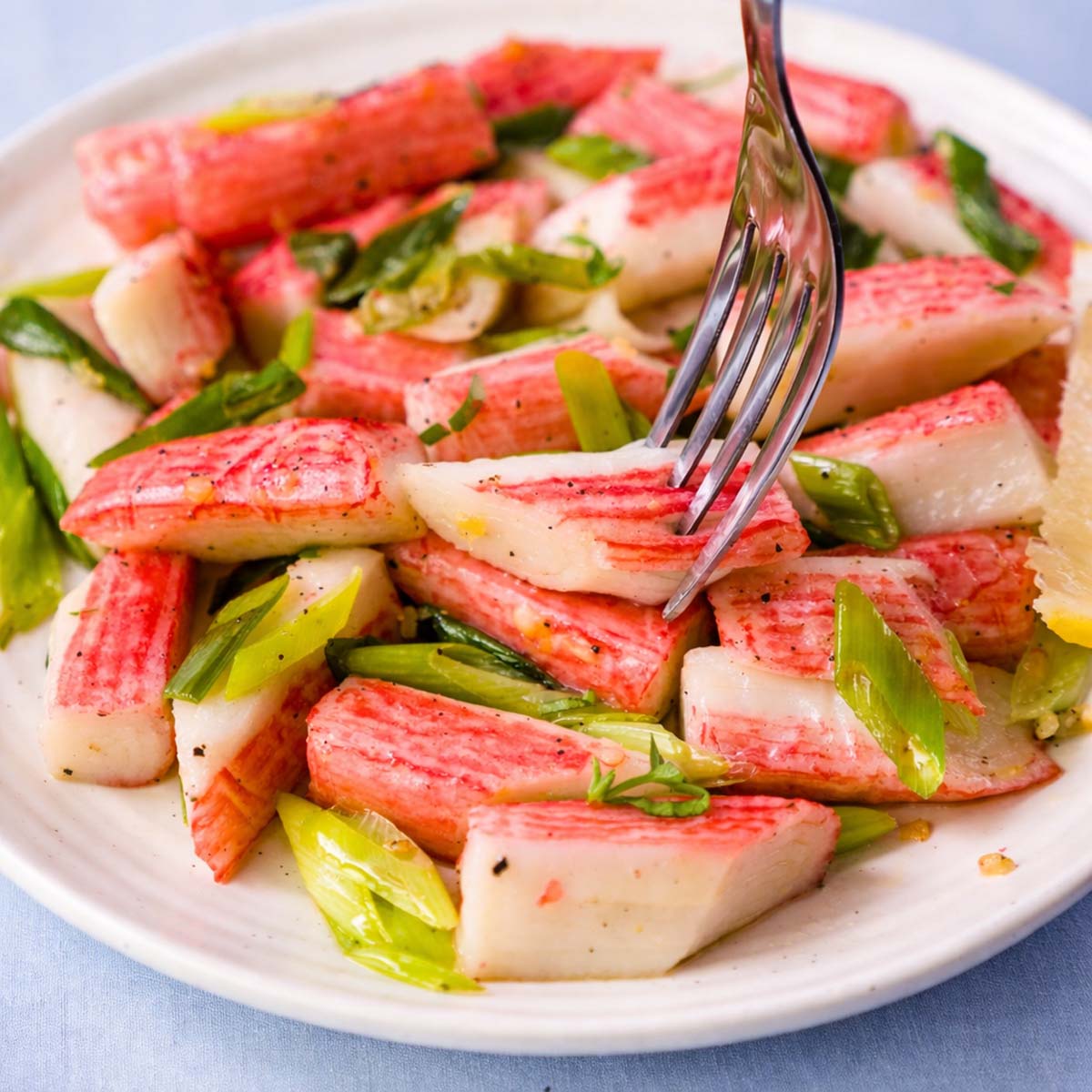 Sauteed imitation crab with garlic butter, green onions, and herbs, served on a white plate with a fork lifting a piece