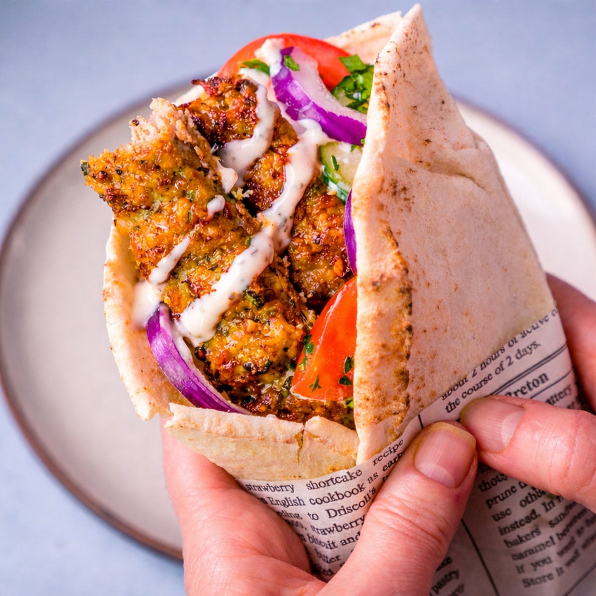 Sheet pan ground chicken kebab wrap in flat bread with tzatziki, tomato, cucumber, and red onion held in hand.