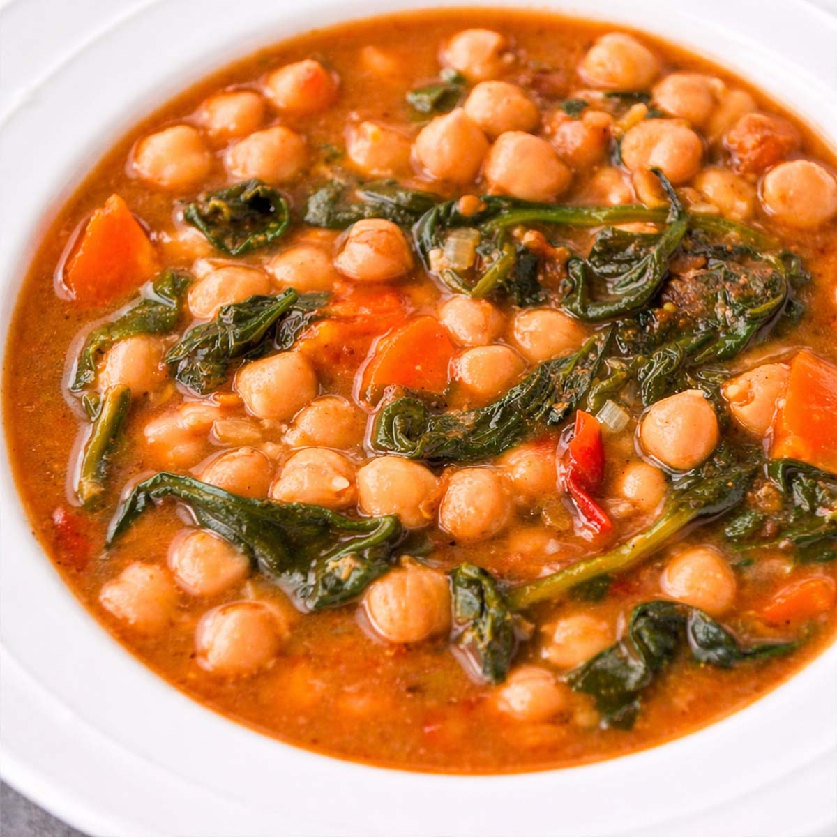 Spanish Chickpea and Spinach Stew (Garbanzos con Espinacas) served in a white bowl with tender chickpeas, wilted spinach, carrots, and a rich tomato-based broth