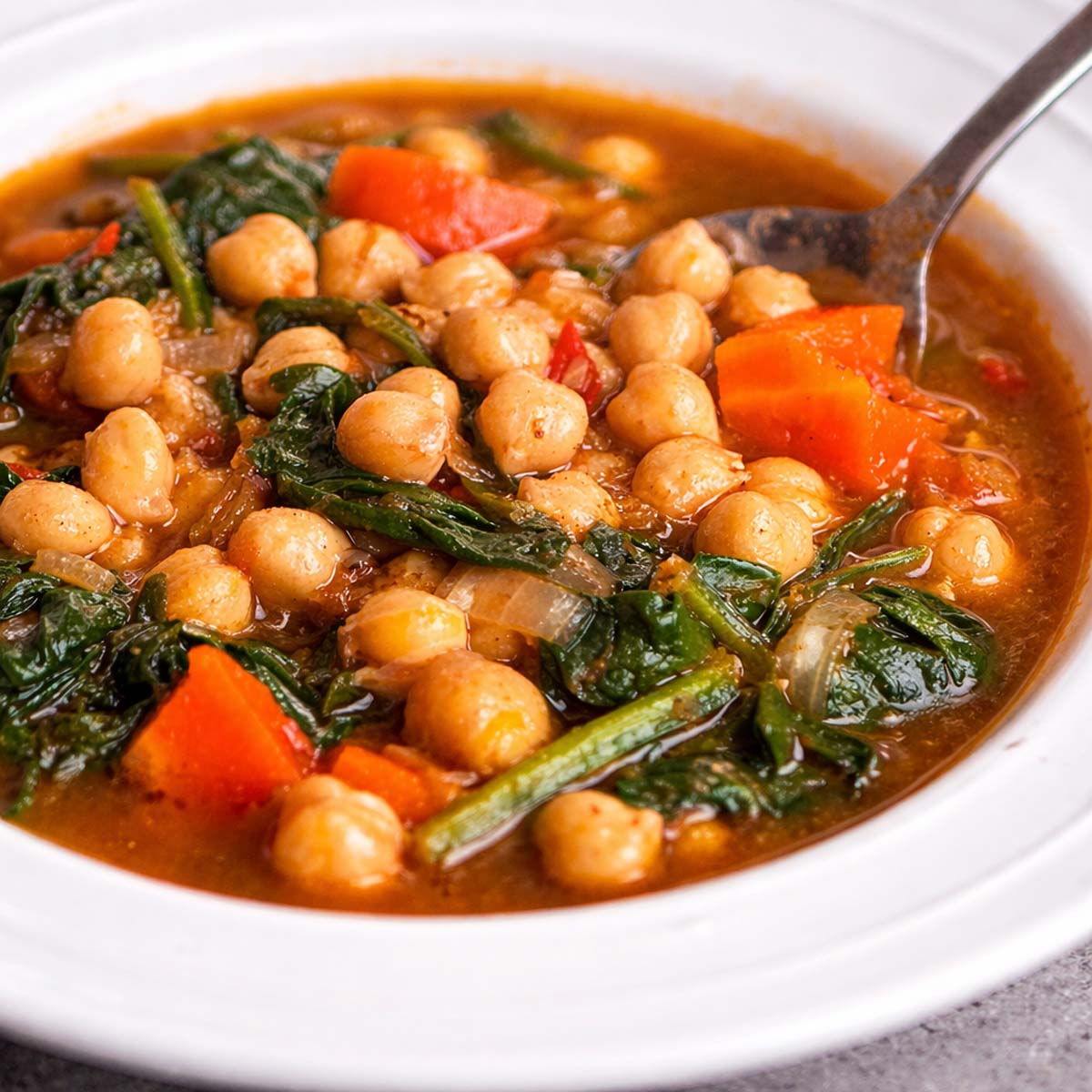 Spanish Chickpea and Spinach Stew (Garbanzos con Espinacas) with chickpeas, spinach, carrots, and tomato broth, served in a white bowl with a spoon