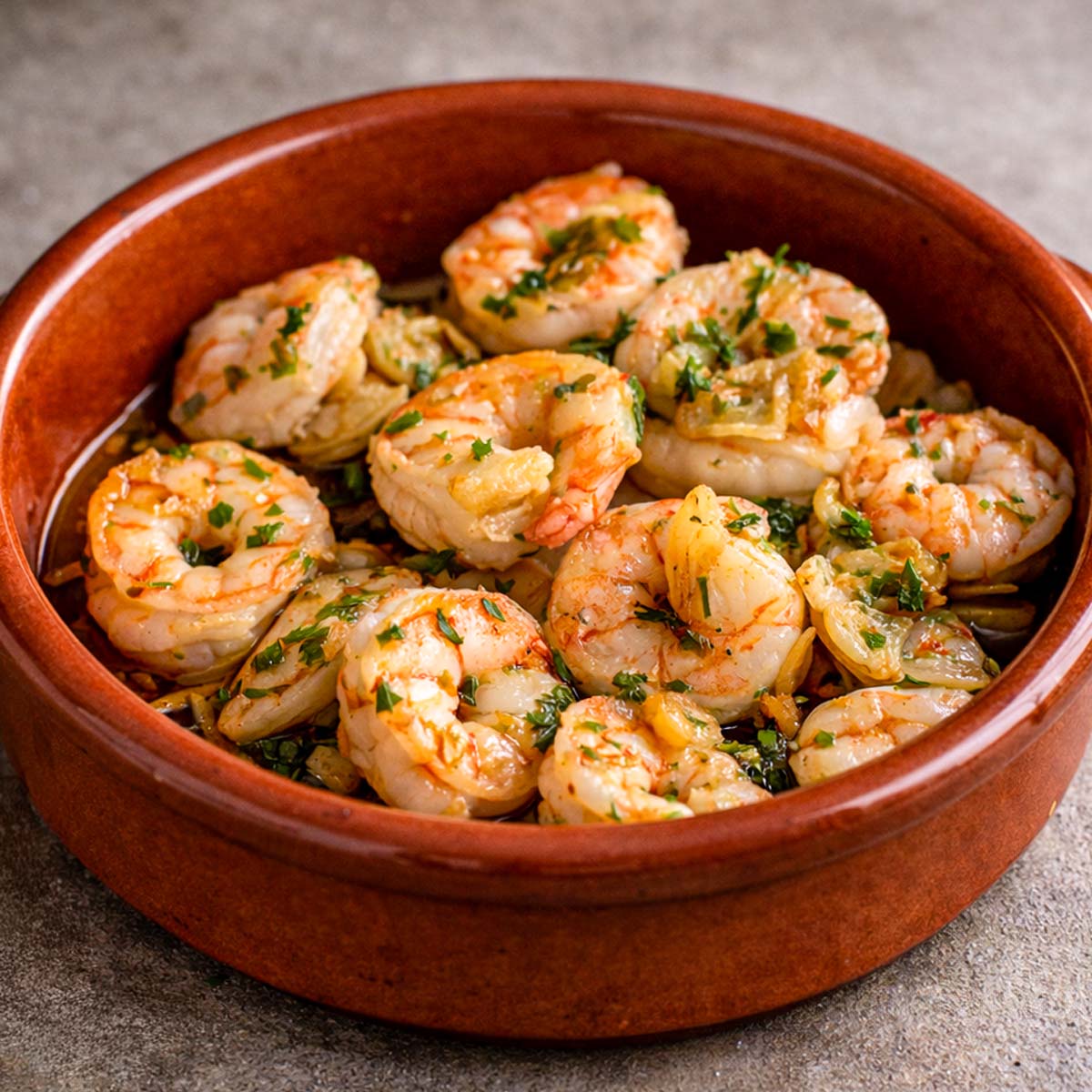 Spanish garlic shrimp gambas al ajillo in a rustic terracotta pan, featuring plump shrimp cooked in olive oil with sliced garlic and fresh parsley