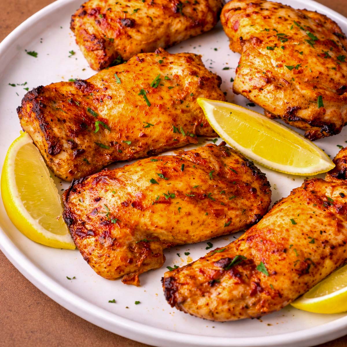 Tomato marinated chicken thighs roasted until golden and juicy, served with lemon wedges and a sprinkle of fresh herbs on a white plate