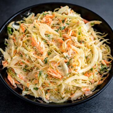 Creamy tuna cabbage salad in a black bowl, made with shredded cabbage, carrots, onion, and herbs in a light yogurt-style dressing.