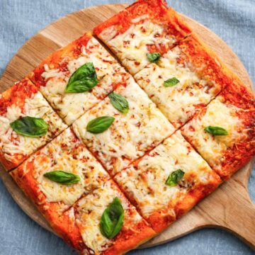Vegan Margherita pizza sliced into squares with melted vegan cheese, tomato sauce, and fresh basil on a wooden board