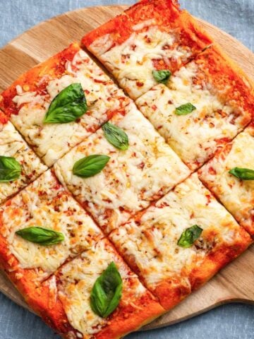 Vegan Margherita pizza sliced into squares with melted vegan cheese, tomato sauce, and fresh basil on a wooden board