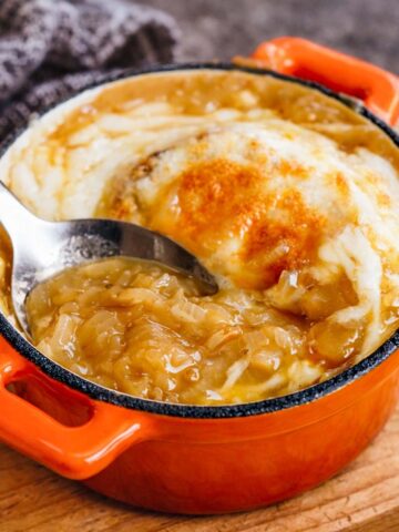 vegetarian french onion soup with caramelized onions and melted gruyere cheese in an orange cast iron pot, close-up