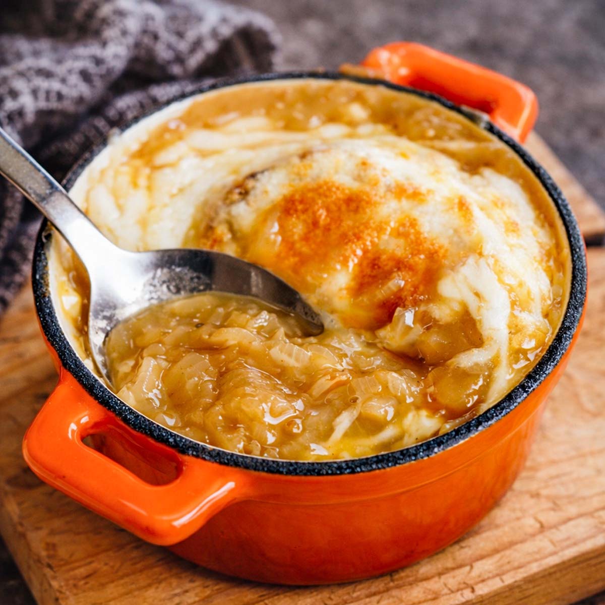 vegetarian french onion soup with caramelized onions and melted gruyere cheese in an orange cast iron pot, close-up