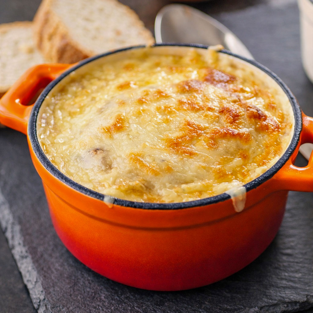 vegetarian french onion soup with caramelized onions and melted gruyere cheese in an orange cast iron pot, close-up