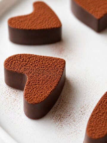 2 Ingredient Chocolate Fudge with Cocoa Powder cut into heart shapes, coated in cocoa and arranged on a white plate