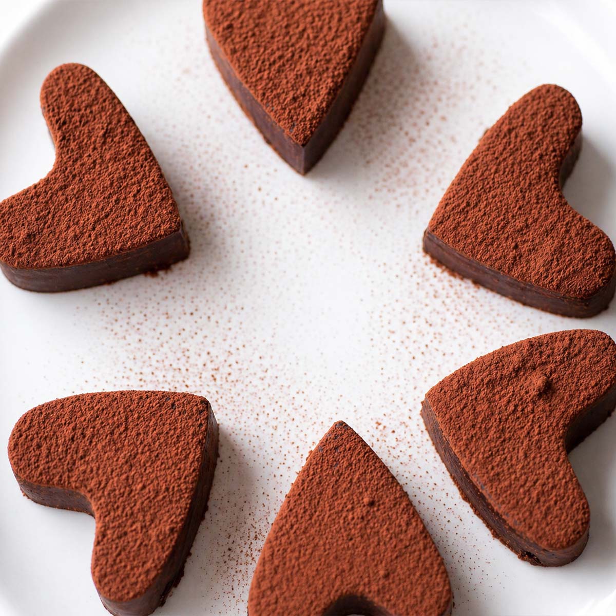 2 Ingredient Chocolate Fudge with Cocoa Powder shaped into hearts, dusted with cocoa powder and arranged in a circle on a white plate