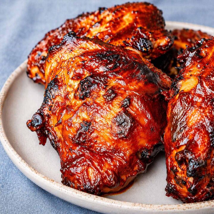 baked BBQ chicken thighs on a plate with glossy caramelized barbecue sauce on a blue linen background