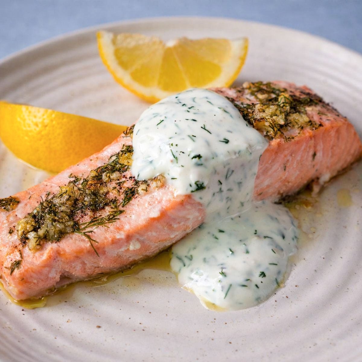 baked lemon dill salmon topped with creamy dill sauce served with lemon wedges on a plate