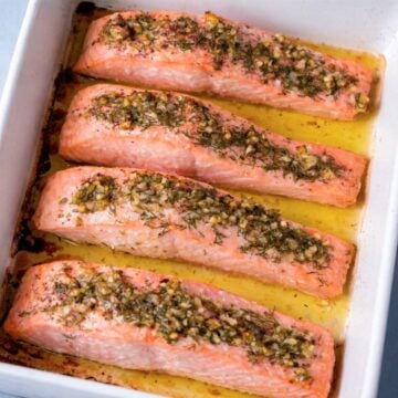baked lemon dill salmon fillets in a white baking dish with garlic, fresh dill, and olive oil juices
