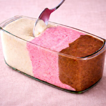 banana nice cream in a glass loaf pan with vanilla, strawberry, and chocolate layers on soft pink linen background
