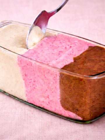 banana nice cream in a glass loaf pan with vanilla, strawberry, and chocolate layers on soft pink linen background