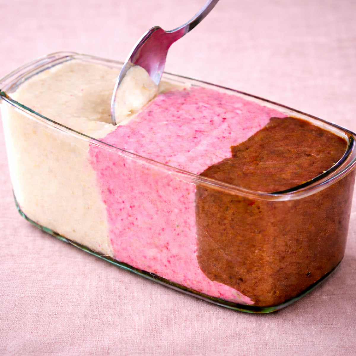 banana nice cream in a glass loaf pan with vanilla, strawberry, and chocolate layers on soft pink linen background