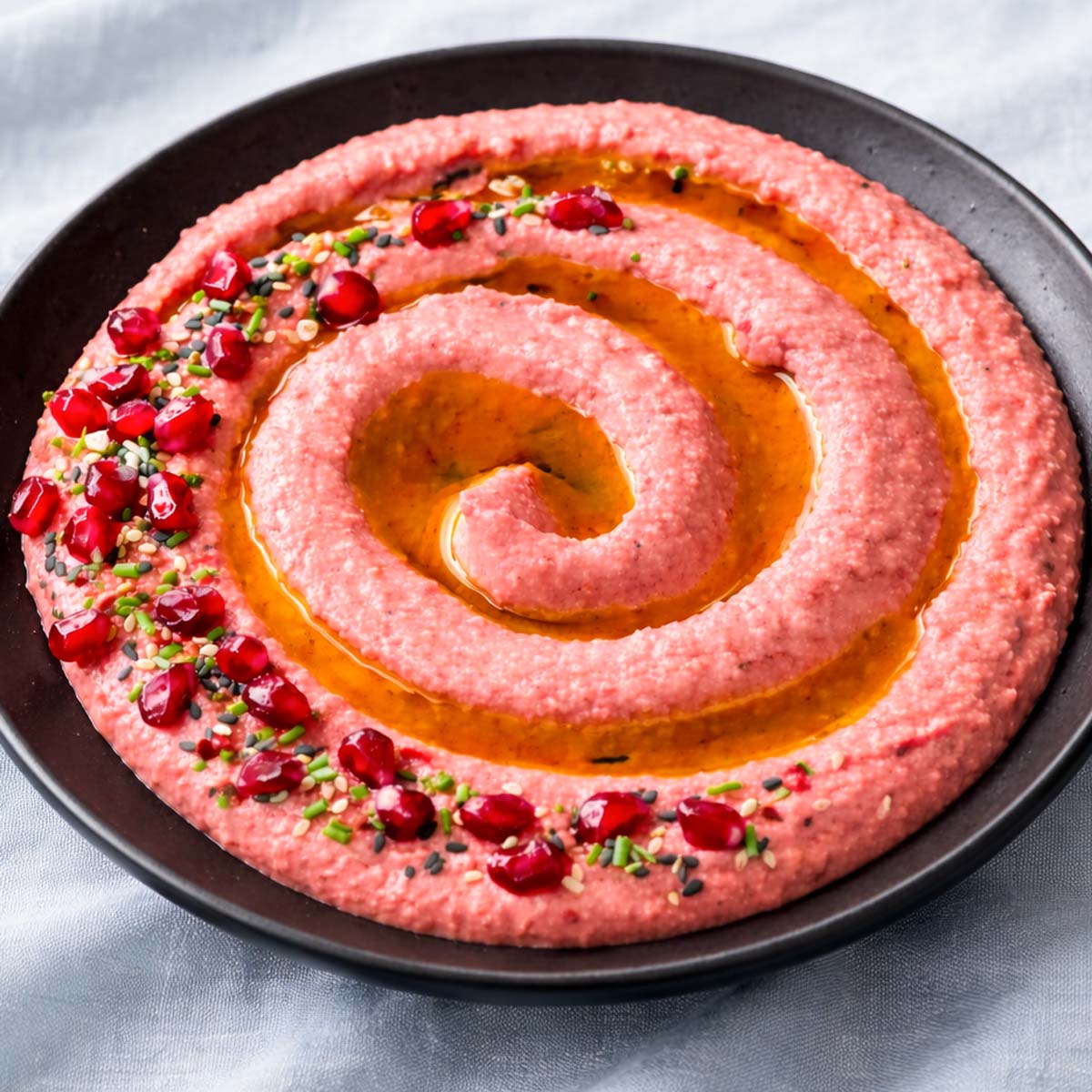 Easy beet hummus with olive oil, pomegranate seeds, sesame, and chives served in a black bowl