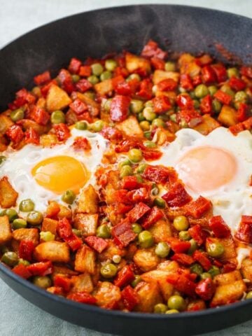 Breakfast hash with eggs and chorizo cooked in a skillet with diced potatoes and peas.