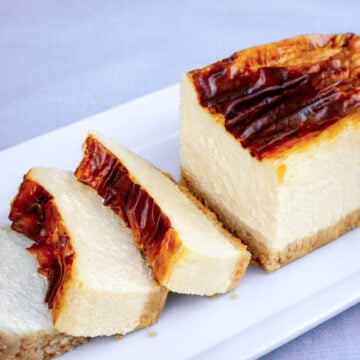 Slice of burnt New York cheesecake with caramelized top and creamy baked cheesecake interior on a white plate