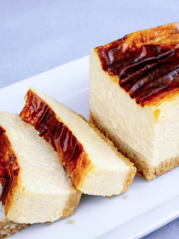Slice of burnt New York cheesecake with caramelized top and creamy baked cheesecake interior on a white plate
