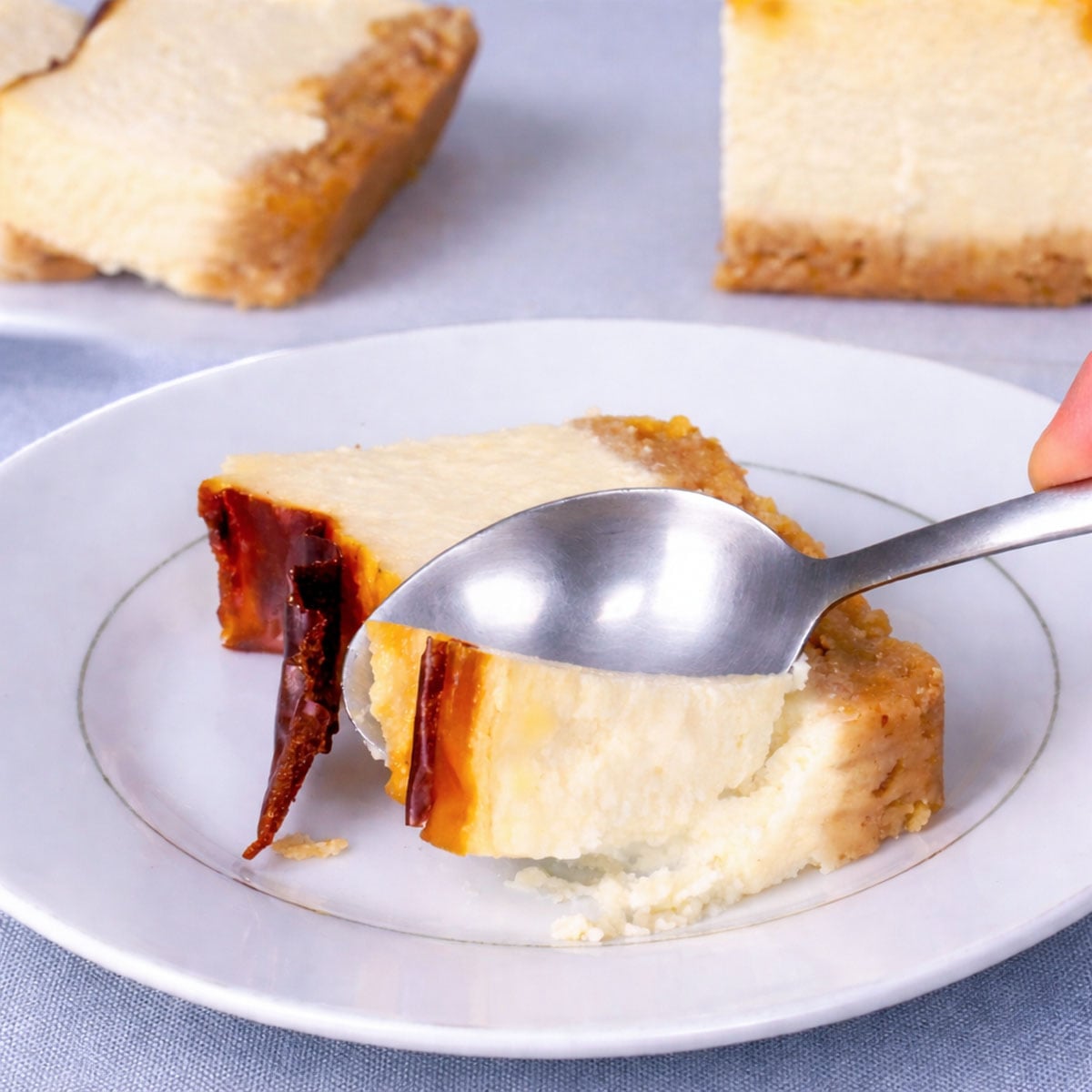 Spoon lifting a bite of burnt New York cheesecake with caramelized top and creamy baked cheesecake texture