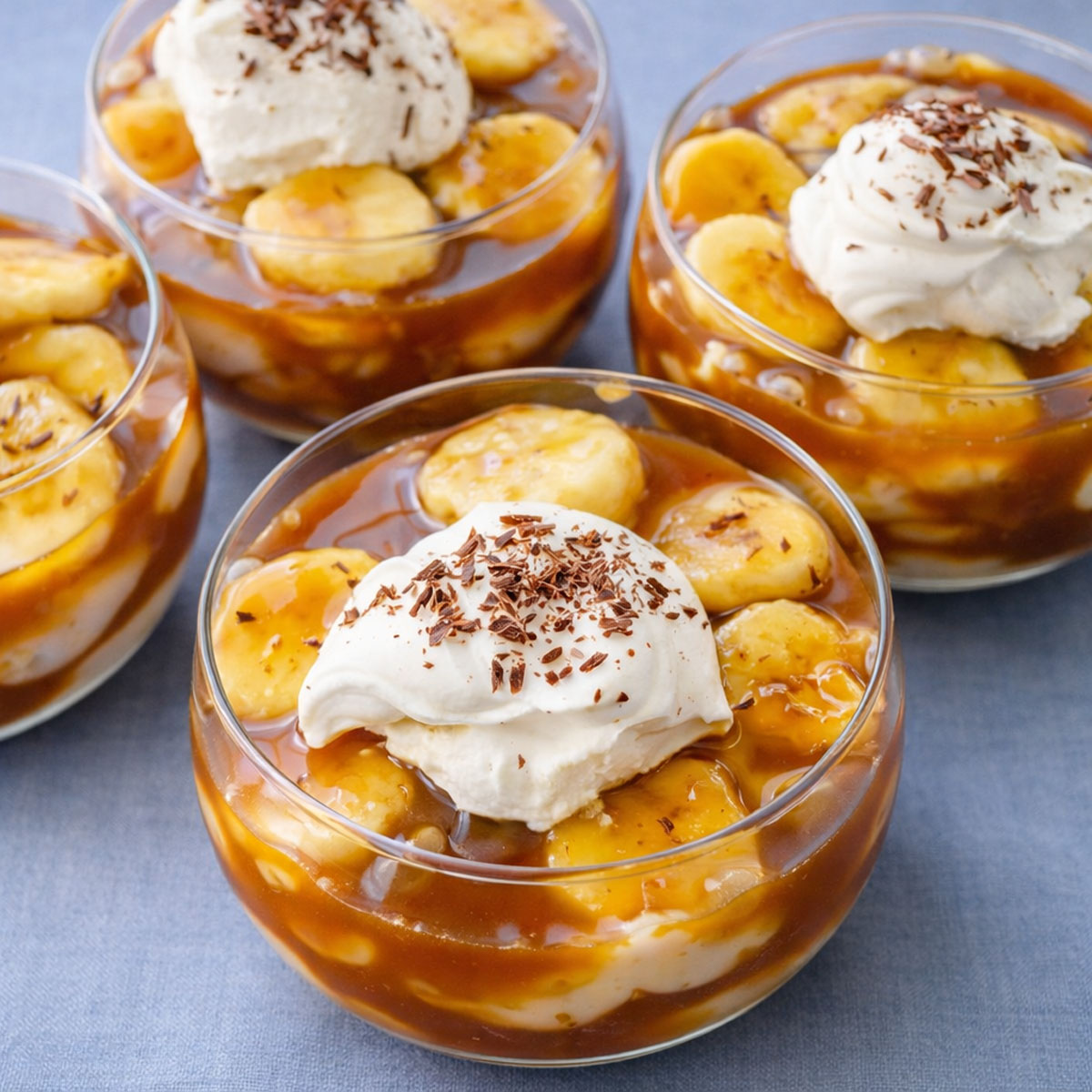 banana caramel pudding cups layered with vanilla custard, sliced bananas, and caramel sauce topped with whipped cream and chocolate shavings