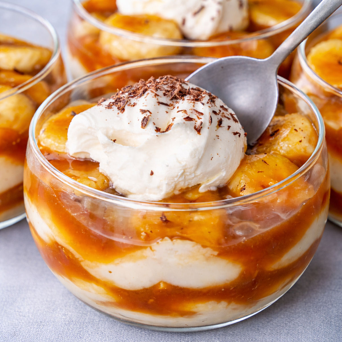 banana caramel pudding with vanilla custard and sliced bananas topped with whipped cream and chocolate shavings in a glass dessert bowl
