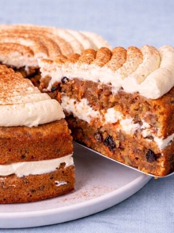 Carrot cake layered with cream cheese frosting and cinnamon on top, with a slice cut out showing the moist carrot and raisin filling.