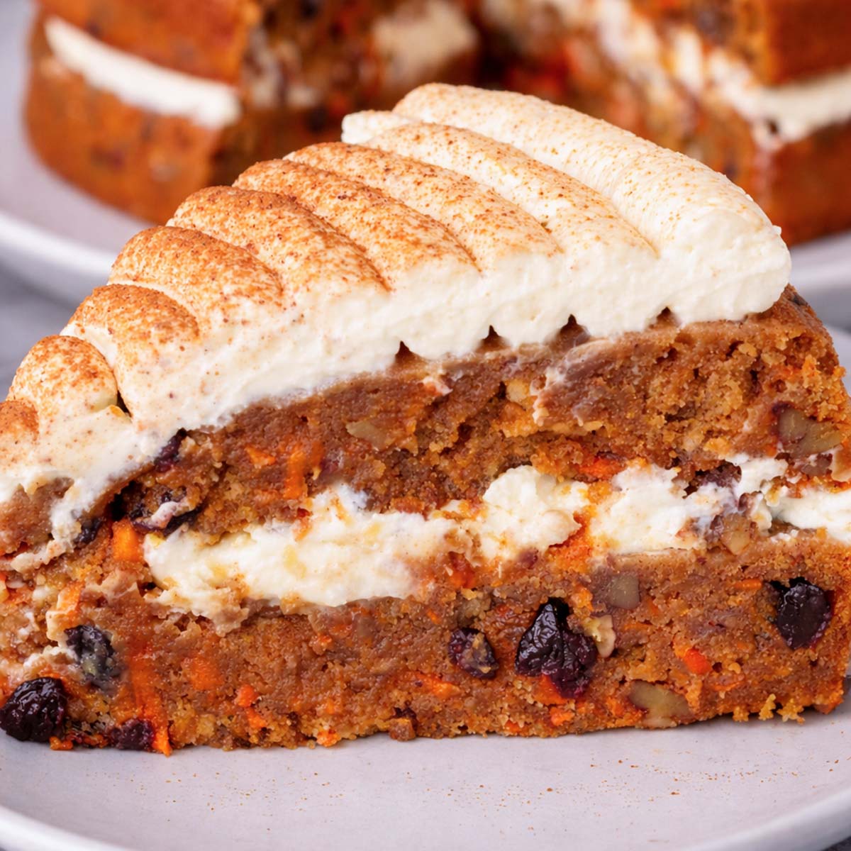 Close up of a piece of Carrot cake layered with cream cheese frosting and cinnamon on top, showing the moist carrot and raisin filling.