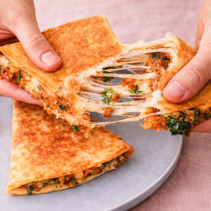 Hands pulling apart crispy cheesy potato quesadillas with melted cheese and potato filling.