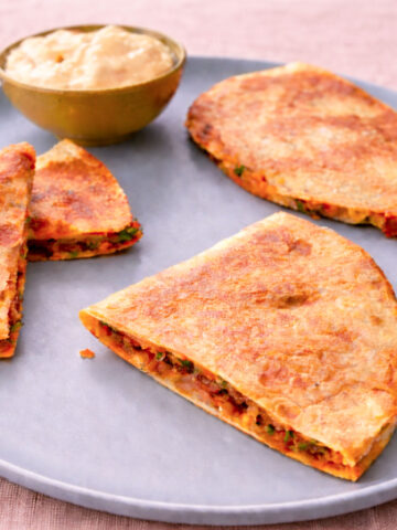 Plate of crispy cheesy potato quesadillas with creamy dipping sauce.
