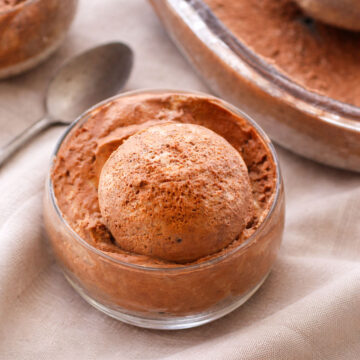 no churn chocolate ice cream in a glass bowl with a smooth creamy scoop, homemade chocolate ice cream dessert close-up on linen background