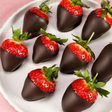 Chocolate dipped strawberries arranged on a white plate with a soft pink background.