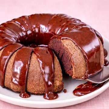 Coca Cola Bundt cake with glossy chocolate glaze on a white plate, moist slice cut and served with a cake server.