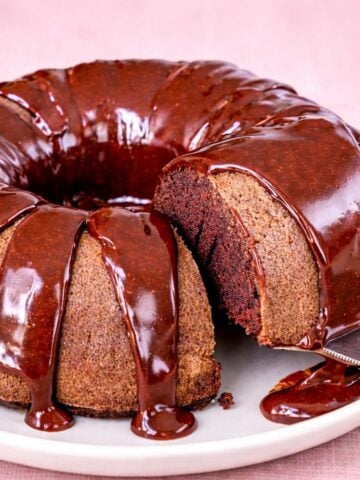 Coca Cola Bundt cake with glossy chocolate glaze on a white plate, moist slice cut and served with a cake server.