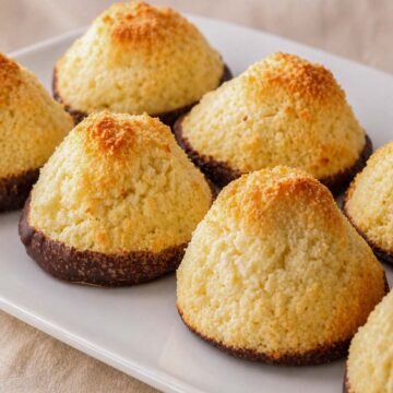Coconut macaroons on a white plate with golden toasted tops and chocolate-dipped bases