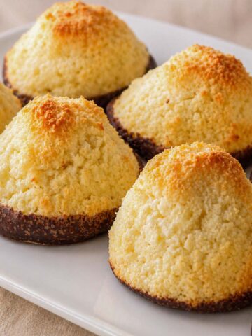 Coconut macaroons on a white plate with golden toasted tops and chocolate-dipped bases