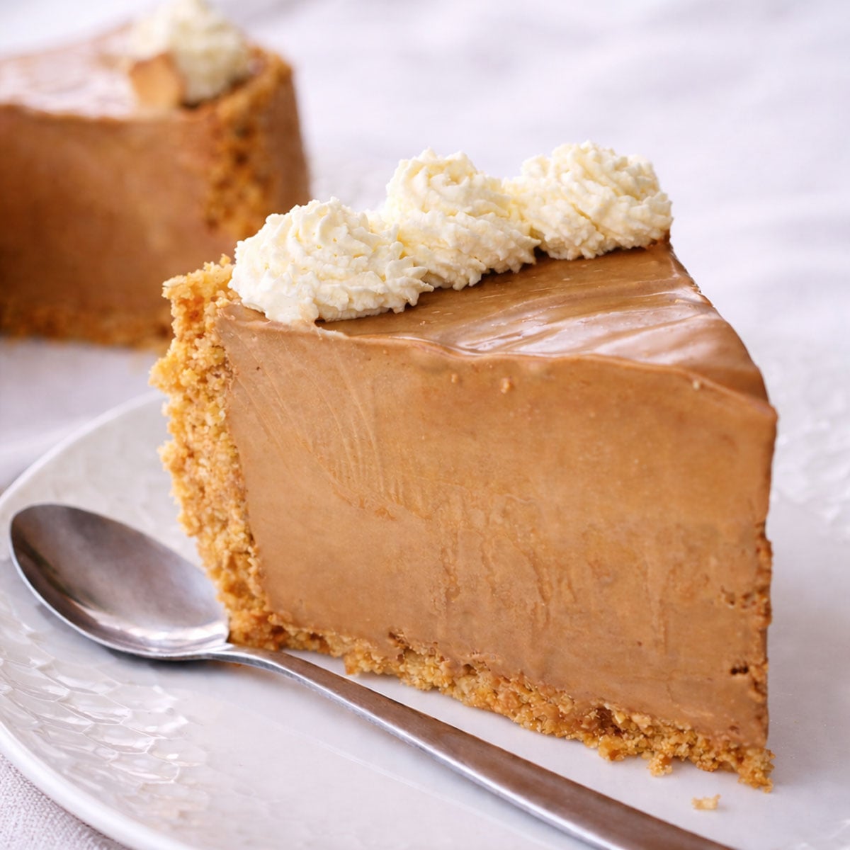 Coffee ice cream cake slice with whipped cream topping and cookies crust on a white plate