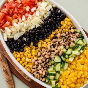cowboy caviar with black beans corn black eyed peas cucumber tomatoes and onion arranged in a bowl